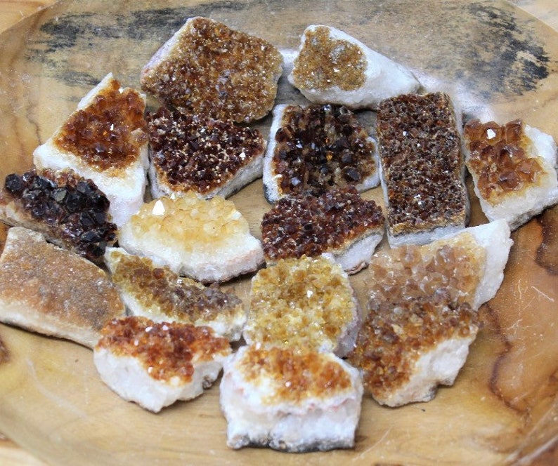 May include: A selection of raw citrine crystal clusters in shades of brown, amber, and yellow, displayed on a wooden surface. The crystals have a rough, textured appearance and vary in size and shape. A natural, earthy product.