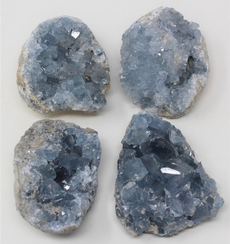 May include: Four celestite crystal clusters. The crystals are a pale blue colour, with a rough, textured exterior. The clusters vary in size and shape, with some showing more defined crystal formations.