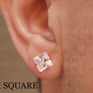 May include: A square-cut, clear gemstone stud earring, approximately 8 mm in size, set in a gold-colored metal. The earring is displayed on an ear. The text "8 MM SQUARE" is visible. The brand name "DI VIOMO" and website address are also visible.