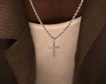 Könnte beinhalten: Eine silberfarbene Kordelkette mit einem schlichten, polierten Kreuzanhänger. Die Metallkette hat ein gedrehtes, strukturiertes Design, das zu einem glatten, einfachen Kreuzanhänger führt, der mittig an einem kleinen Verbindungsring hängt.