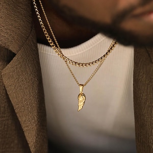 May include: A gold-toned layered necklace set featuring two distinct chains. The shorter chain is a classic curb link, while the longer chain features a delicate pendant shaped like a single feathered wing with detailed texture and a polished finish.
