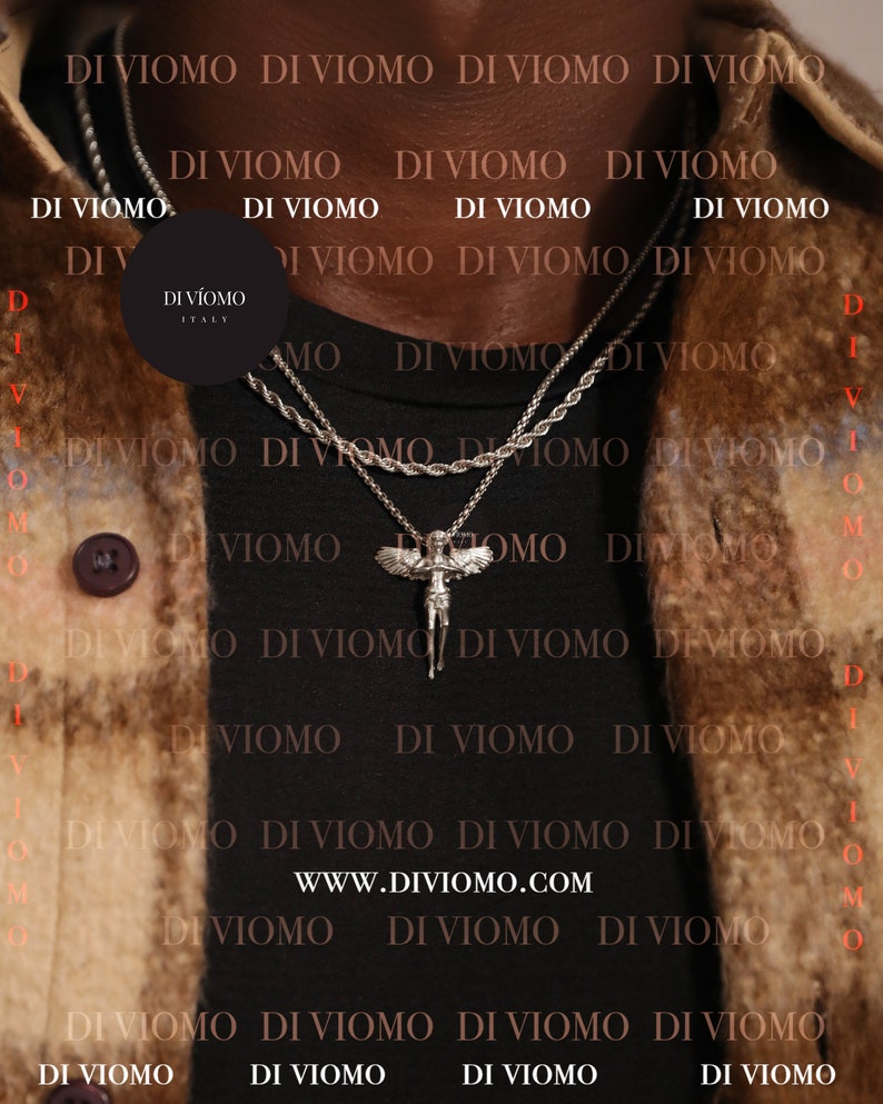 May include: A black shirt with a silver chain necklace featuring an angel pendant. The necklace is layered with a second silver chain. The shirt has the text "DI VIOMO" repeated in a pattern.