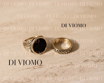 May include: Two gold-toned rings featuring the text DI VIOMO and WWW.DIVIOMO.COM. One ring has a circular black inlay with a textured, leaf-like pattern on the band. The second ring features a braided or twisted rope design around the entire band.