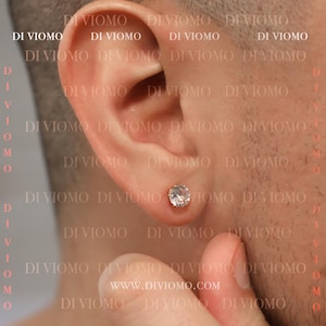 Könnte beinhalten: Nahaufnahme eines Ohrs mit einem kleinen, runden, klaren Diamant-Ohrstecker. Der Ohrstecker ist in einer goldenen Fassung gefasst.