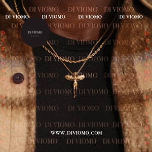 Puede incluir: Una camisa negra con un collar de cadena dorada con un colgante de &aacute;ngel alado. La camisa tiene el texto "DI VIOMO" repetido en la parte delantera. El texto "WWW.DIVIOMO.COM" tambi&eacute;n es visible en la camisa.