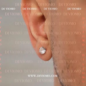 May include: A close-up of a person's ear with a single silver earring featuring a large, clear, round cubic zirconia stone.