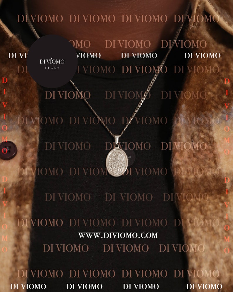 May include: A silver chain necklace with a silver pendant featuring a religious image. The necklace is worn by a person wearing a brown jacket. The background is a black and brown pattern with the text "DI VIOMO" repeated.