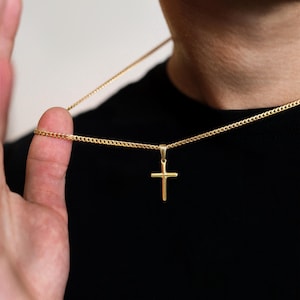 May include: A gold-toned cross pendant suspended from a matching gold-toned curb chain necklace. The cross features a simple, smooth design with a polished finish, hanging vertically from a small bail attached to the thin, interlocking metal links.