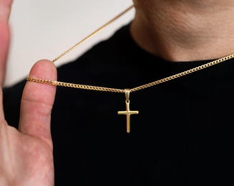 May include: A gold-toned cross pendant suspended from a matching gold-toned curb chain necklace. The cross features a simple, smooth design with a polished finish, hanging vertically from a small bail attached to the thin, interlocking metal links.