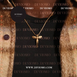 May include: A gold chain necklace with a pendant featuring a winged angel figure. The necklace is worn by a person wearing a black shirt with the text "DI VIOMO" repeated in white.