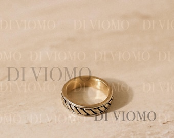 May include: A gold-toned metal ring featuring a central band with a repeating diagonal rope-like texture. The ring has smooth, polished edges on the top and bottom. The text DI VIOMO is repeated across the background of the image.