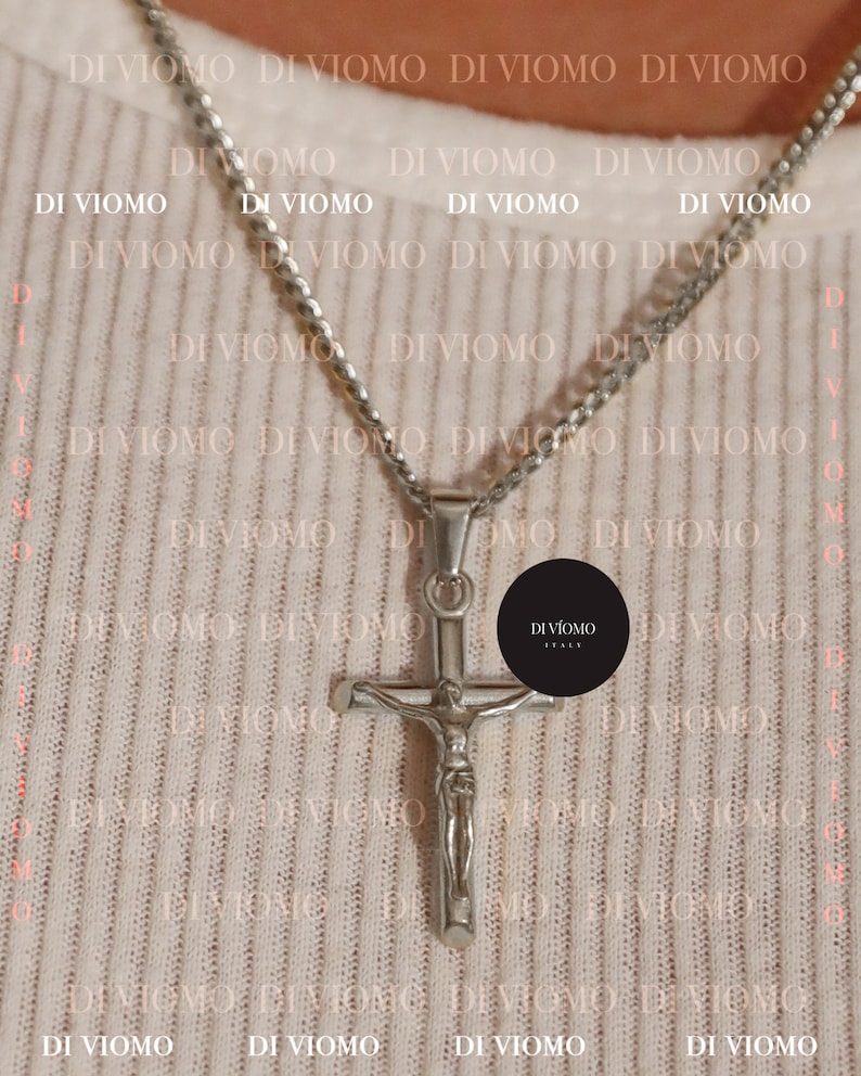 Puede incluir: Un collar de cadena de plata con un colgante de cruz de plata. La cruz presenta una figura de Jesucristo. El collar est&aacute; sobre un fondo blanco con el texto "DI VIOMO ITALY" repetido.