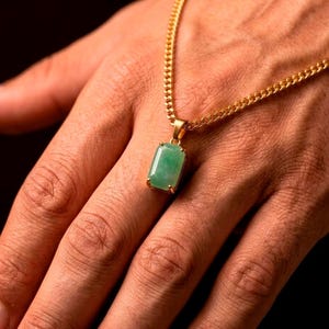 May include: A gold-toned chain necklace featuring a rectangular, light green stone pendant held in a four-prong setting. The pendant hangs from a classic curb link chain, showcasing a polished metallic finish and a smooth, translucent green gemstone.