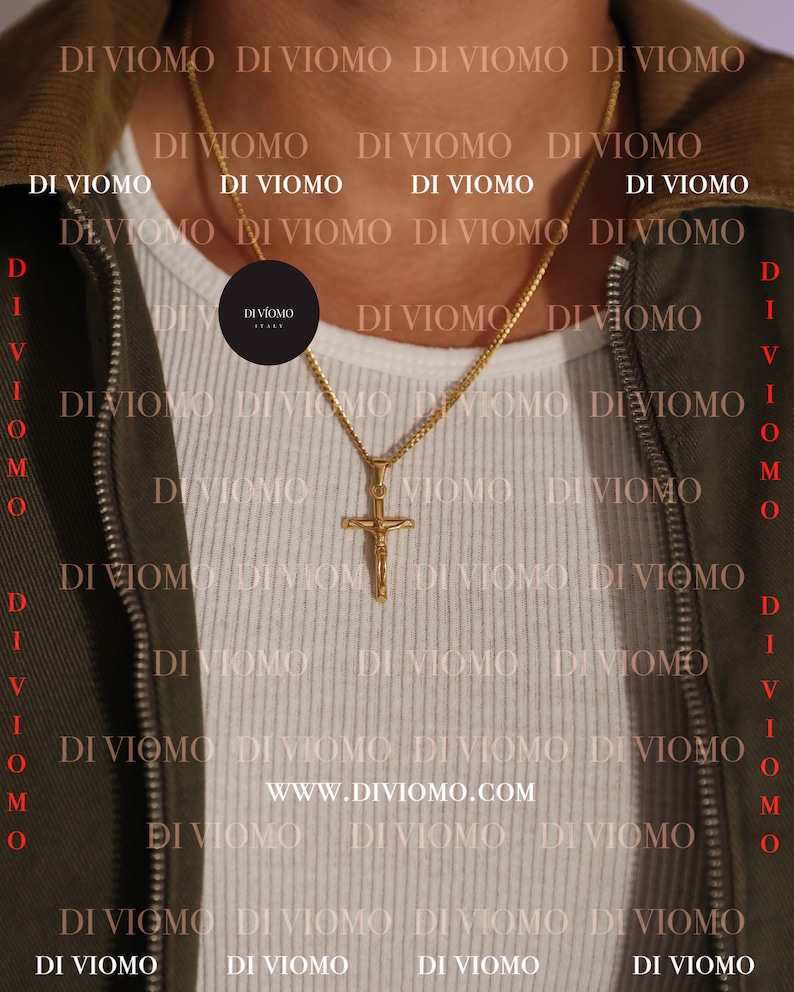 May include: A gold chain necklace with a gold cross pendant. The cross features a figure of Jesus Christ. The necklace is worn by a person wearing a white shirt and a green jacket. The text "www.diviomo.com" is visible on the shirt.