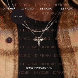 May include: A black shirt with a silver chain necklace featuring an angel pendant. The necklace is layered with a second silver chain. The shirt has the text "DI VIOMO" repeated in a pattern.