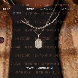 May include: A black shirt with a silver chain necklace featuring a pendant with a detailed design. The shirt has the text "DI VIOMO" repeated across the front. The text "DI V&Iacute;OMO ITALY" is on a black circle tag on the shirt.