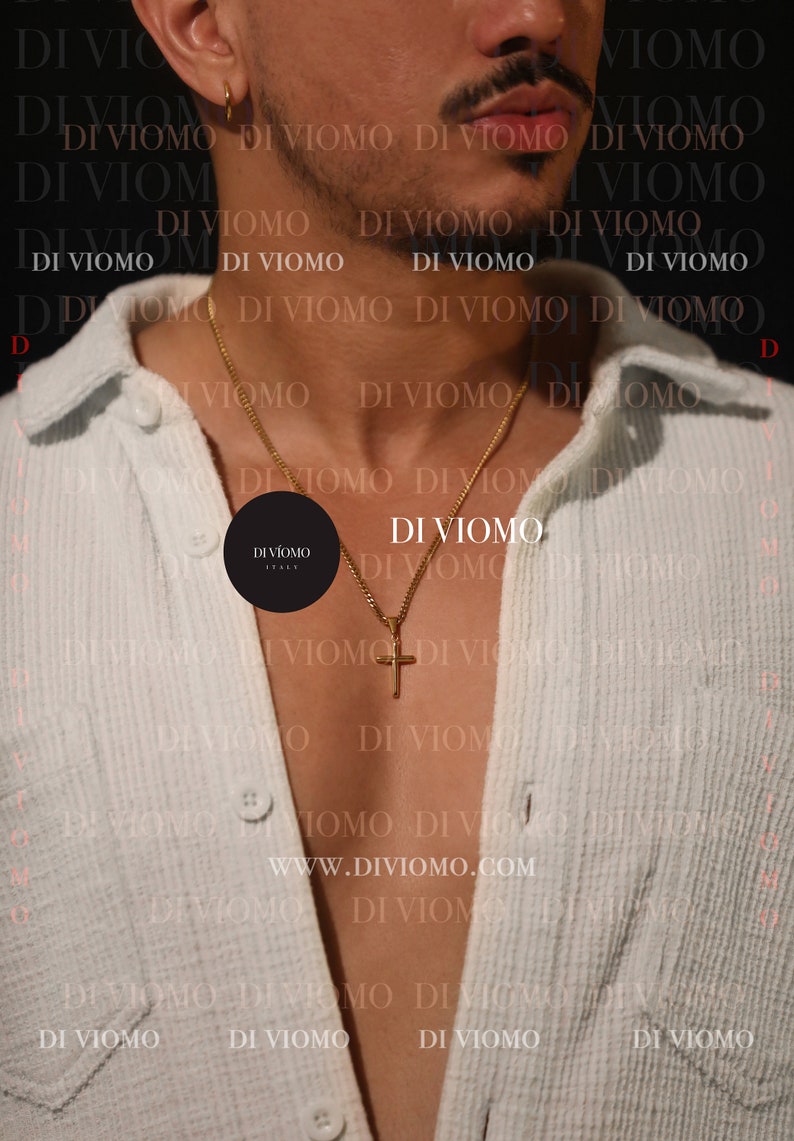 May include: A gold chain necklace with a small cross pendant. The necklace is worn by a person wearing a light blue shirt. The text "DI VIOMO" is repeated in the background.