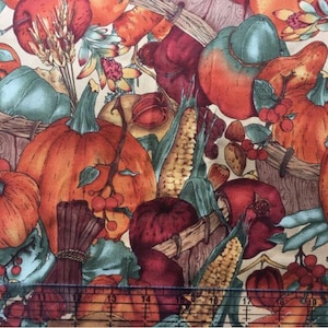 May include: A colorful fabric featuring a pattern of pumpkins, corn, and other autumnal elements. The fabric is a cream color with orange, red, green, and brown accents.