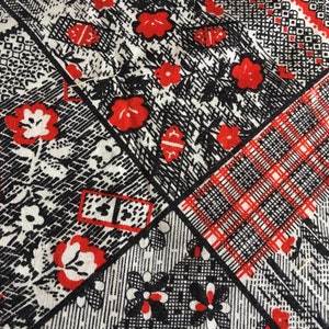 May include: Close-up of a fabric with a patchwork design. The pattern features red floral and geometric elements on a white and black background. The design includes squares with floral, plaid, and abstract patterns.