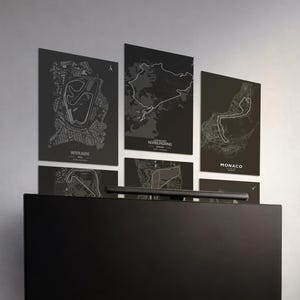 May include: A collection of black and white racing circuit maps, including Interlagos, Nurburgring, and Monaco, displayed on a wall. The maps feature detailed track layouts and are mounted above a black surface.
