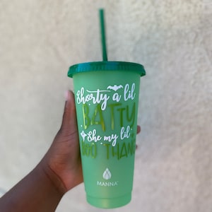 May include: A green reusable cup with a white design that says "shorty a lil batty she my lil boo thang" and a green lid. The cup has a green straw and a white logo that says "MANNA".