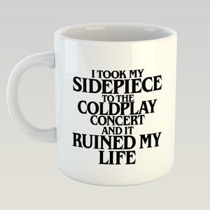 May include: White ceramic mug with a curved handle. The mug features black text that reads: "I TOOK MY SIDEPIECE TO THE COLDPLAY CONCERT AND IT RUINED MY LIFE."
