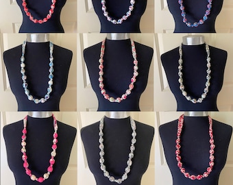 May include: Nine fabric necklaces with different floral patterns and colors. Each necklace is made of fabric beads and is displayed on a mannequin.