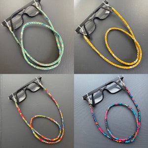 May include: Four pairs of glasses with different patterned eyeglass chains. The chains are made of fabric and feature floral patterns in green, yellow, red, and blue.
