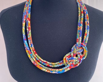 May include: A multi-strand necklace made of fabric with a floral print in shades of blue, red, green, and white. The necklace is tied in a knot at the front.