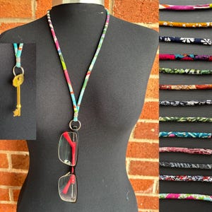 May include: A patterned lanyard with glasses and a key. The lanyard features a floral design in pink, blue, and green. The glasses have a black frame with red arms. A gold key hangs from a small loop.