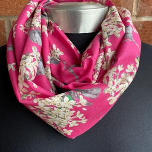May include: A pink infinity scarf with a white floral print and small birds.