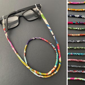 May include: Black eyeglasses with a colorful fabric eyeglass chain. The chain features a vibrant pattern of pink, blue, yellow, and green. A selection of other patterned chains are displayed to the right.