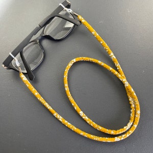 May include: A pair of black eyeglasses with a mustard yellow and white floral patterned eyeglass strap.