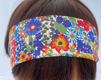 May include: A white headband with a floral print featuring red, orange, yellow, blue, and green flowers. The headband is made of fabric and is suitable for women.