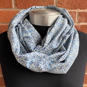 May include: A white infinity scarf with a blue floral pattern. The scarf is made of a soft, lightweight fabric and is perfect for adding a touch of style to any outfit.