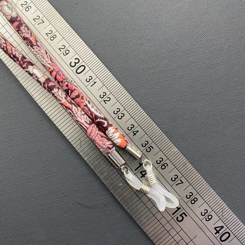 May include: Two floral patterned eyeglass chains with silver metal clasps. The chains are measured against a ruler, showing they are approximately 35 inches long.