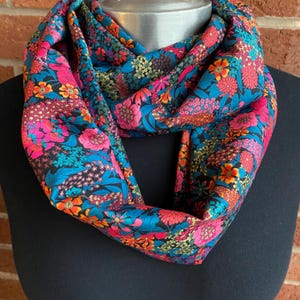May include: A black infinity scarf with a colorful floral print featuring pink, orange, blue, and green flowers on a black background.