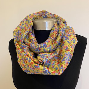 May include: A yellow infinity scarf with a floral pattern in shades of blue, red, and pink.