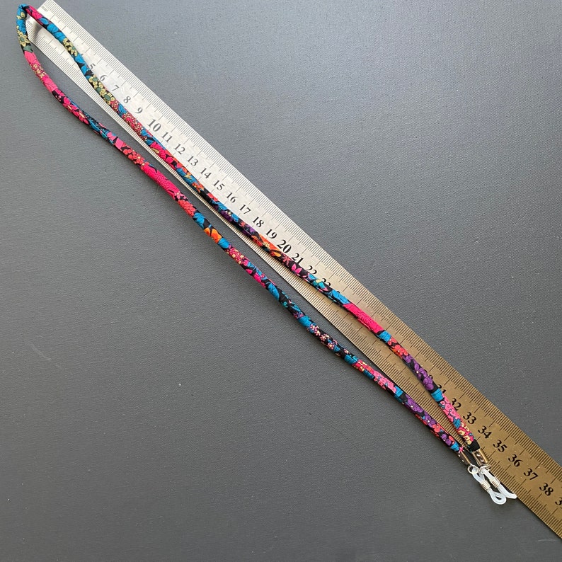 May include: A colorful patterned glasses chain with black, pink, blue, and white floral designs. The chain is approximately 38 inches long and has metal clasps at each end.