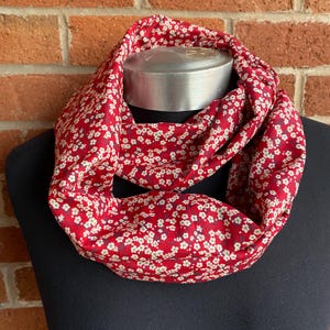 May include: A red infinity scarf with a white floral pattern. The scarf is made of a soft, comfortable fabric and is perfect for adding a touch of style to any outfit.