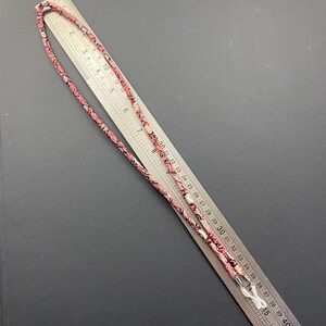 May include: A pink and white patterned eyeglass chain with a metal clasp. The chain is approximately 30 inches long.