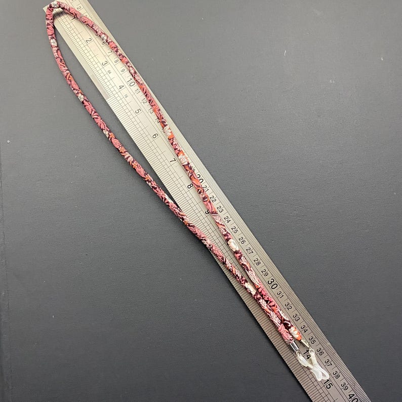 May include: A pink and white patterned eyeglass chain with a metal clasp. The chain is approximately 30 inches long.