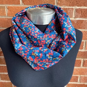 May include: A blue infinity scarf with a floral pattern featuring red, white and yellow flowers on a dark blue background.