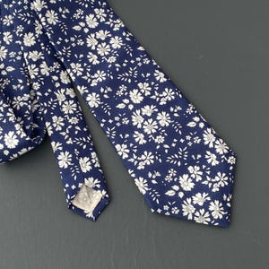 May include: A navy blue tie with a white floral pattern. The tie has a pointed tip and is made of a smooth fabric.