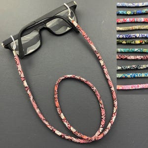 May include: A pair of black eyeglasses with a floral patterned eyeglass chain. The chain is pink, white, and brown with a floral design.