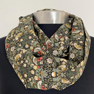 May include: A green infinity scarf with a floral and bird print. The print features small red berries, green leaves, and white flowers.