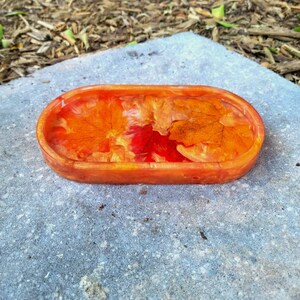 May include: An oval-shaped resin tray with a clear, glossy finish. The tray features embedded fall leaves in shades of orange, red, and yellow.
