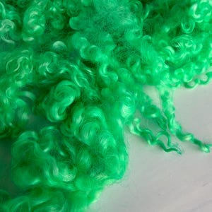 May include: A pile of vibrant, bright green curly fiber locks. The material features a distinct, tight, and springy texture with a glossy sheen, showcasing individual ringlets and soft, tangled strands of neon green wool or synthetic hair.