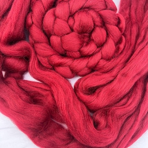 May include: Close-up of vibrant red wool roving, arranged in a spiral and flowing strands. The thick, textured fibers create a visually appealing display, perfect for fiber art projects like needle felting or wet felting. The rich color adds warmth.