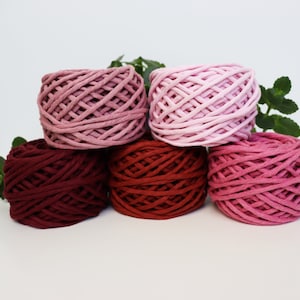 May include: Four spools of cotton rope yarn in shades of pink and red. The yarn is wound into a circular shape and is ready for crafting projects.